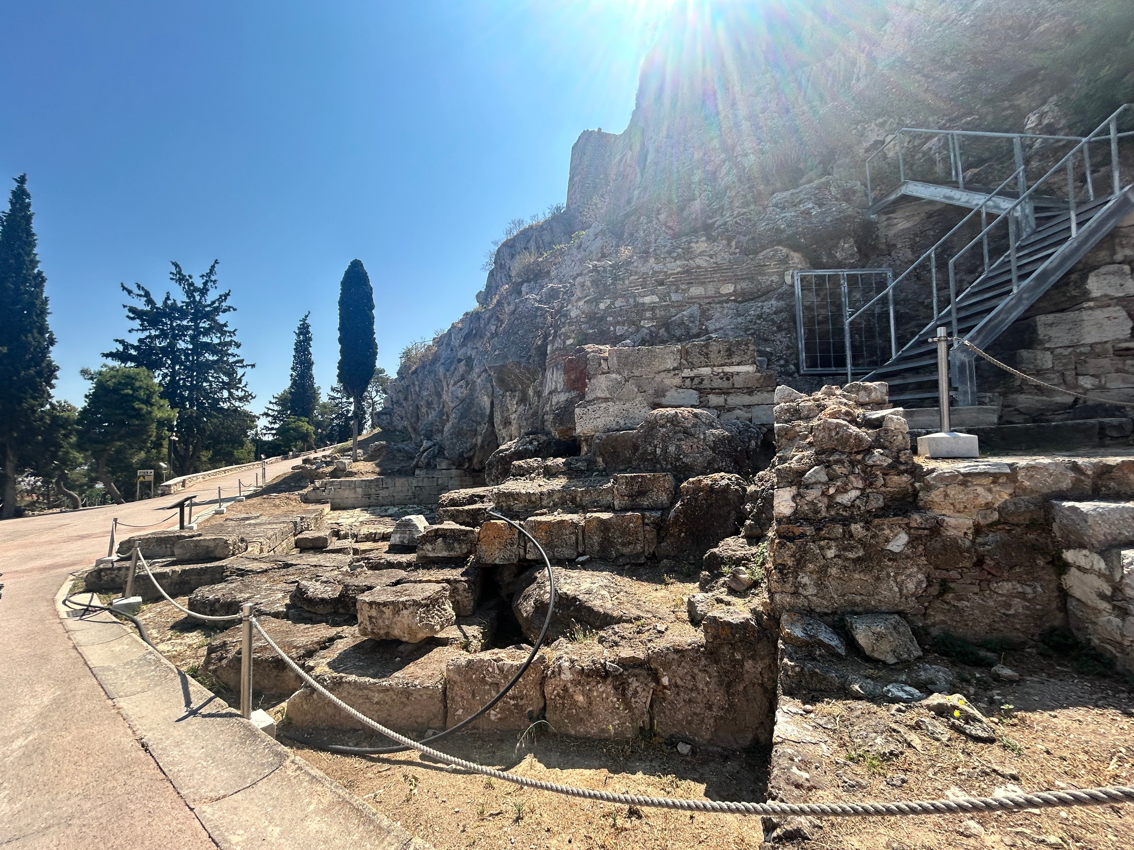 Ancient Acropolis ruins with a roped walkway and cliff in the background